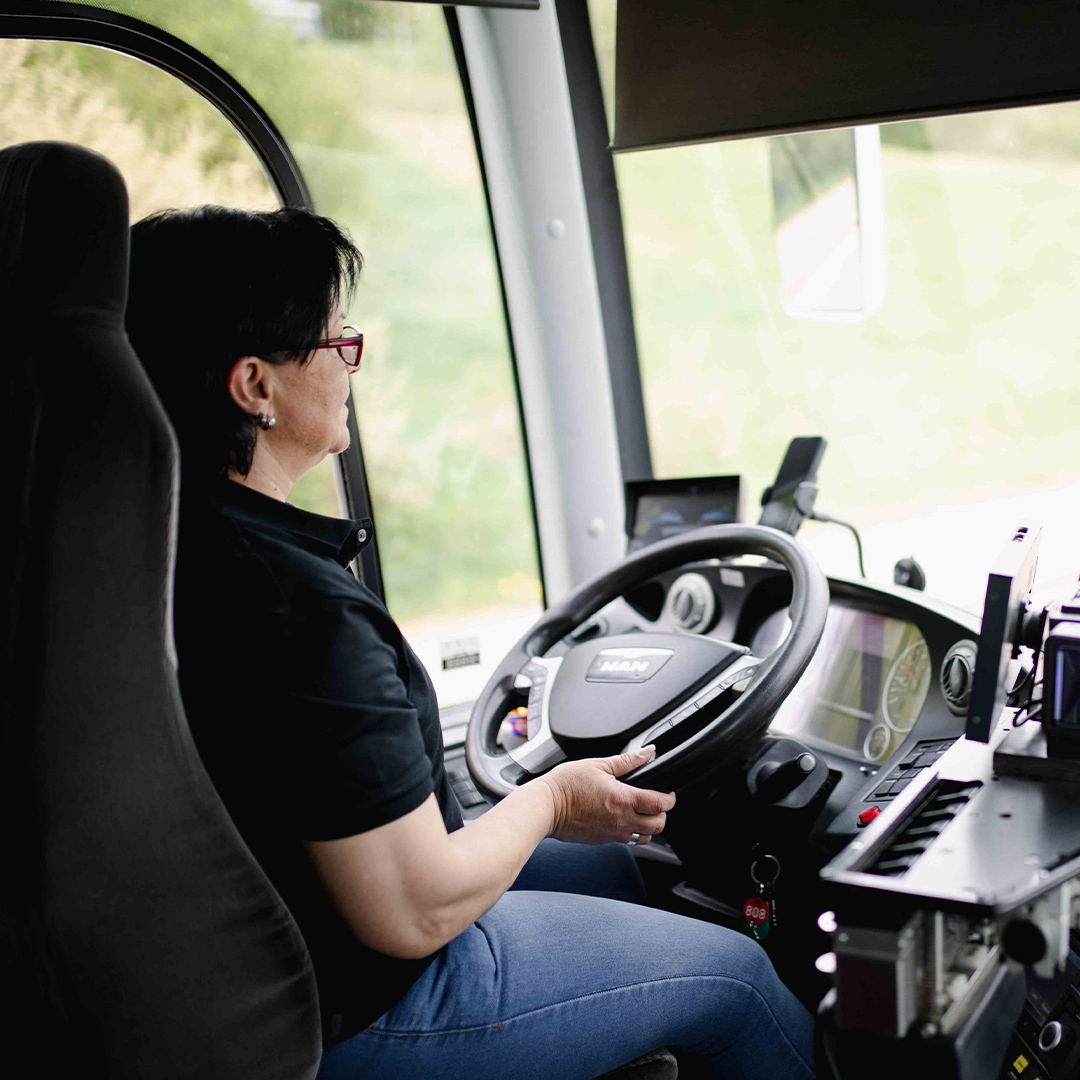 Frau von hinten zu sehen, die am Steuer eines Busses sitzt.