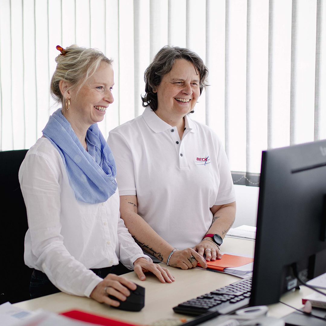 Zwei Frauen stehen am Schreibtisch und schauen in den Computer.