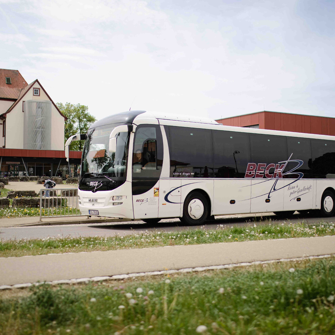 Bus steht vor einem Gebäude an einer Haltestelle.